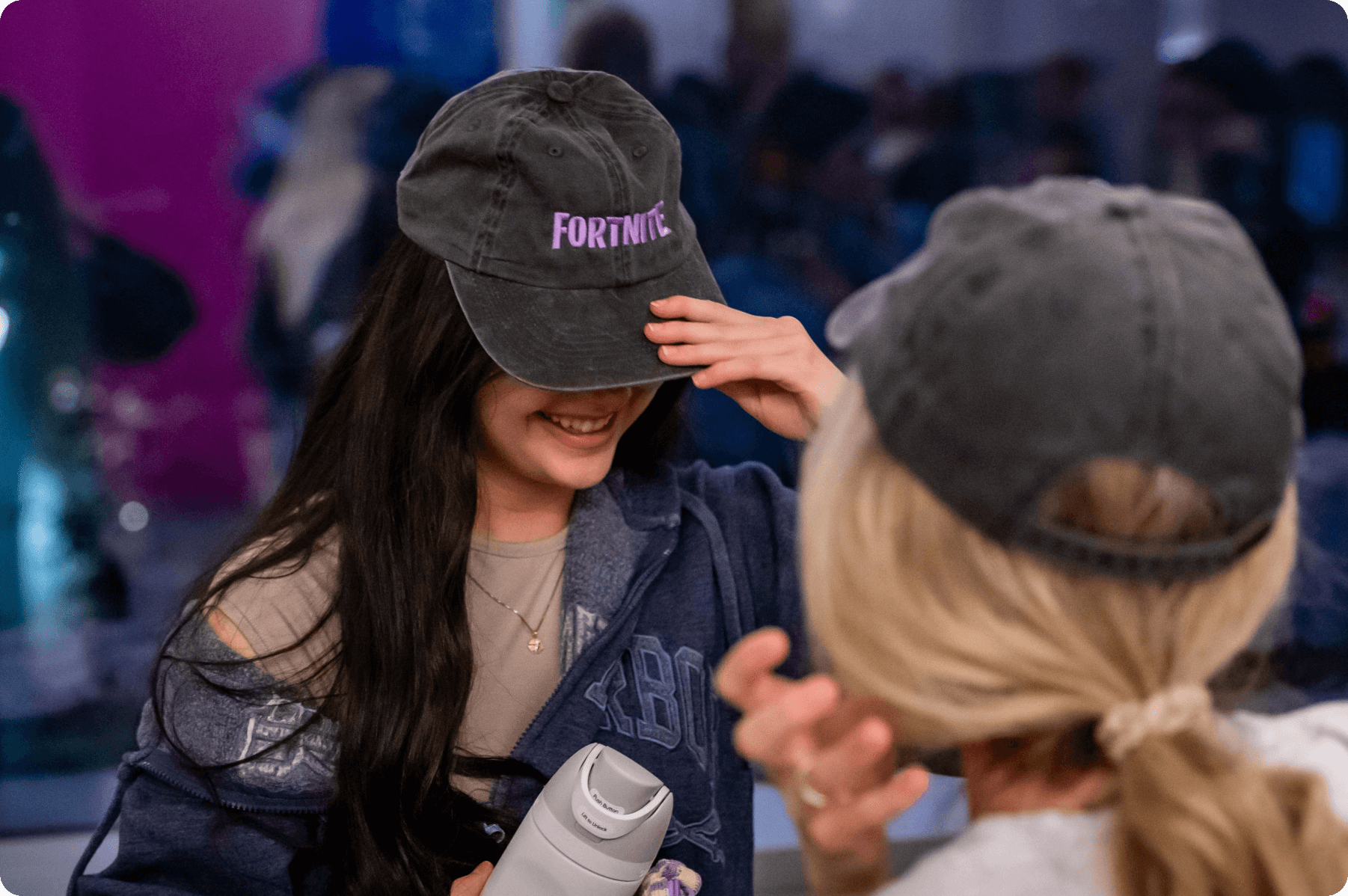 2 woman wear hats with the Fortnite logo.