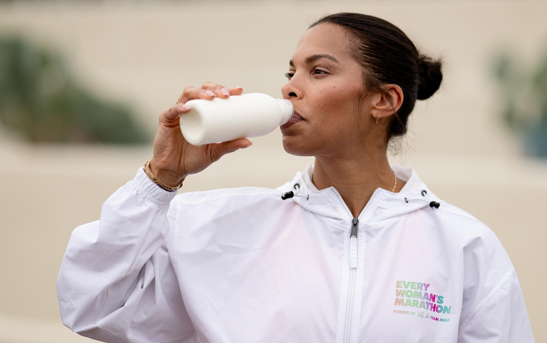 Two women sitting alongside the Chicago River holding up glass bottles of chocolate milk in celebration, Chicago skyline in the background.