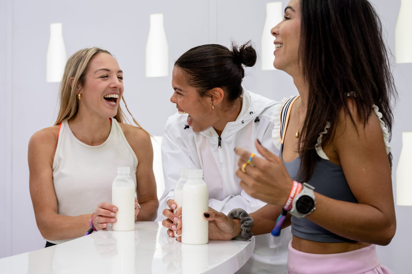 Three women laugh together while holding bottles of milk.</p>
<p>